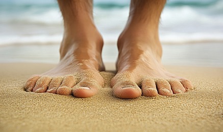 A closeup of feet lying on the beach, with sand and ocean waves